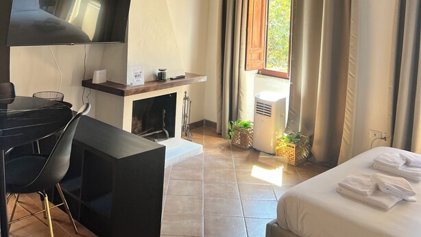 Een kamer met een houten plafond, een flatscreen televisie, een bureau met een stoel, een bed met handdoeken en een raam met gordijnen.
