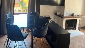Een eethoek met een ronde tafel, twee stoelen, een aan de muur bevestigde televisie en een open haard.