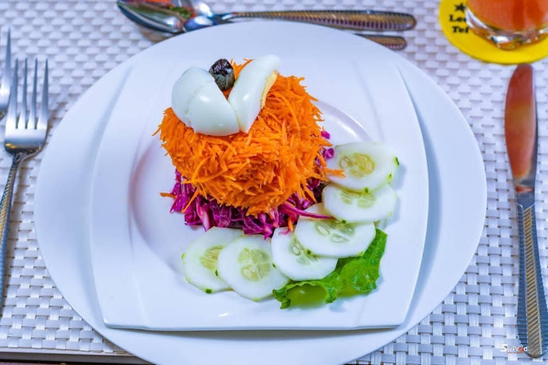 A plate of salad with shredded carrots, sliced cucumbers, and a boiled egg on a white plate.