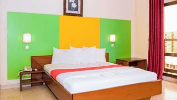 Habitación de hotel con cama de madera, paredes decoradas en tonos verde y amarillo, cortina roja y un cuadro en la pared.