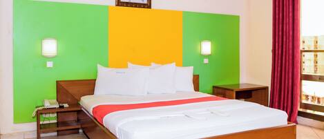 Habitación de hotel con cama de madera, paredes decoradas en tonos verde y amarillo, cortina roja y un cuadro en la pared.