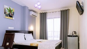 Una habitación de hotel con cama, escritorio, silla, televisor y una pequeña kitchenette.