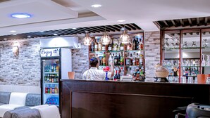 Zona de bar con asientos, un cantinero y una variedad de botellas y vasos en estanterías.