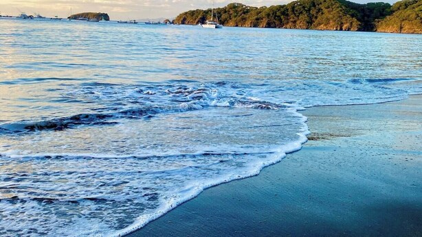 Ein Strand mit Wellen, eine entfernte Insel und ein klarer Himmel.
