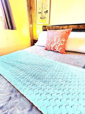 A bed with a blue patterned bedspread and a coral coral-patterned pillow. - Beach Front Cottage - Head on the cloud, toes on the sand (Port Lavaca)