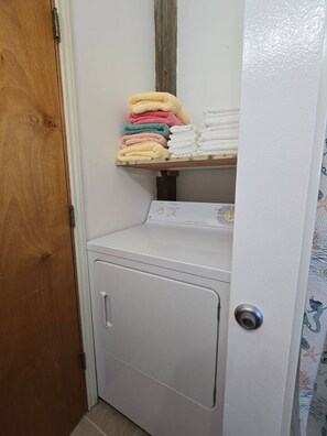A laundry area with a washing machine and a shelf with folded towels. - Beach Front Cottage - Head on the cloud, toes on the sand (Port Lavaca)
