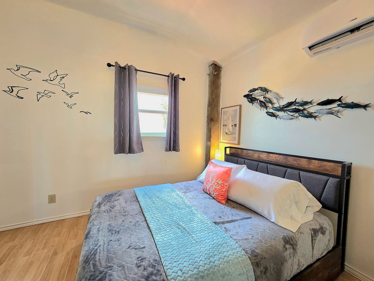 A bedroom with a bed, curtains, wall art, and an air conditioning unit.