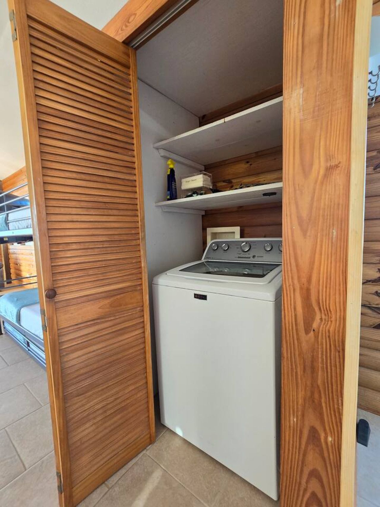 A compact laundry room with a washing machine and dryer, wooden shelving, and a sliding door.