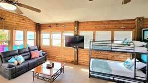 Um quarto acolhedor com sofá, beliches, televisão e paredes de madeira.