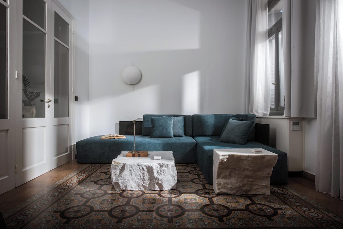 A modern living room with a blue sofa, a white coffee table, and a patterned rug.