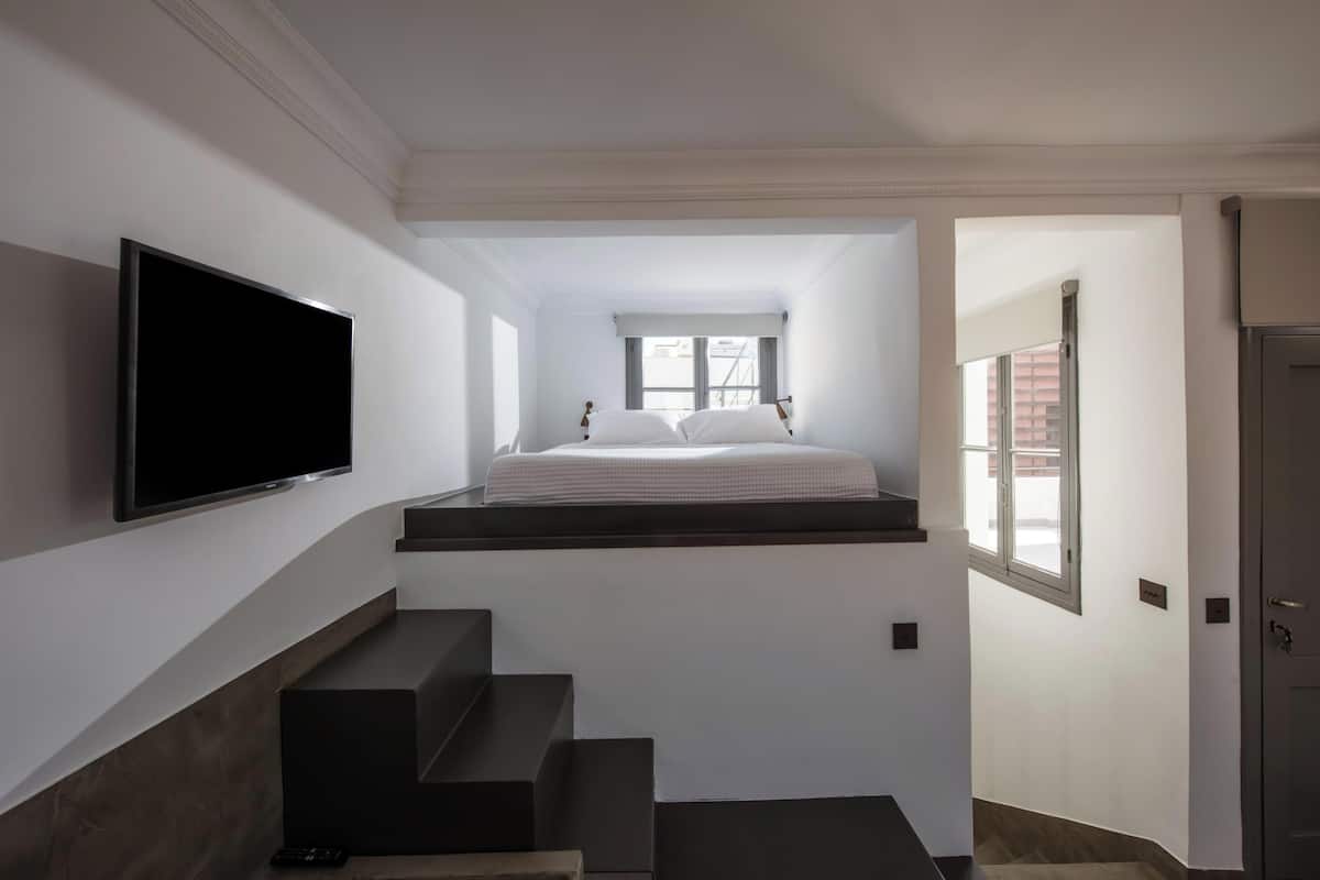 A bedroom with a bed, a TV mounted on the wall, and a staircase leading to a loft area.