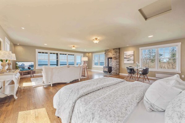 Une chambre spacieuse avec un grand lit, une cheminée en pierre, un coin repas et une vue sur l’extérieur.