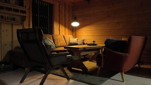 A cozy cabin interior with a wooden ceiling, a sofa, a dining table, and a chair.