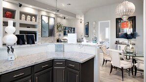 A modern kitchen with dark cabinetry, a granite countertop, and a dining area with a glass table and white chairs. - Zen Den Scottsdale: 2 King Suites Heated pool/Spa/Grill steps away (Scottsdale)
