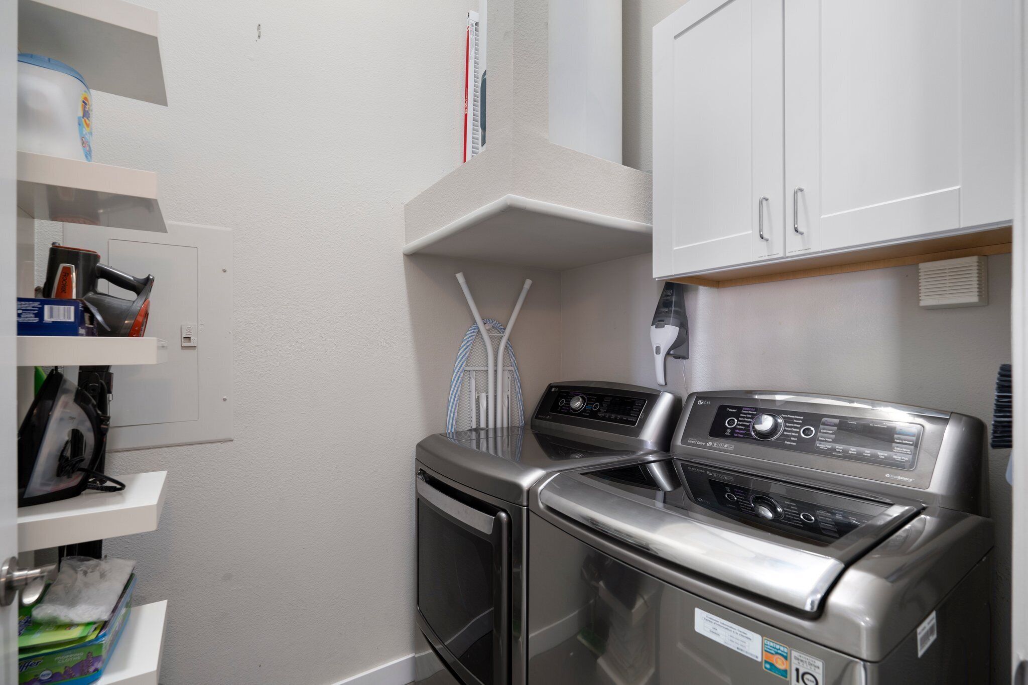 Un espace buanderie comprenant un lave-linge et un sèche-linge, une étagère avec des produits de nettoyage et un mur blanc.