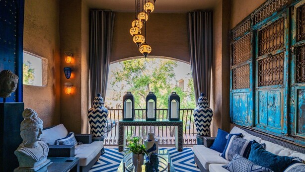 A cozy lounge area with a sofa, a coffee table with decorative items, and a view of a courtyard with a decorative gate and trees. - Zen Den Scottsdale: 2 King Suites Heated pool/Spa/Grill steps away (Scottsdale)