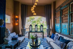 A cozy lounge area with a sofa, a coffee table with decorative items, and a view of a courtyard with a decorative gate and trees.