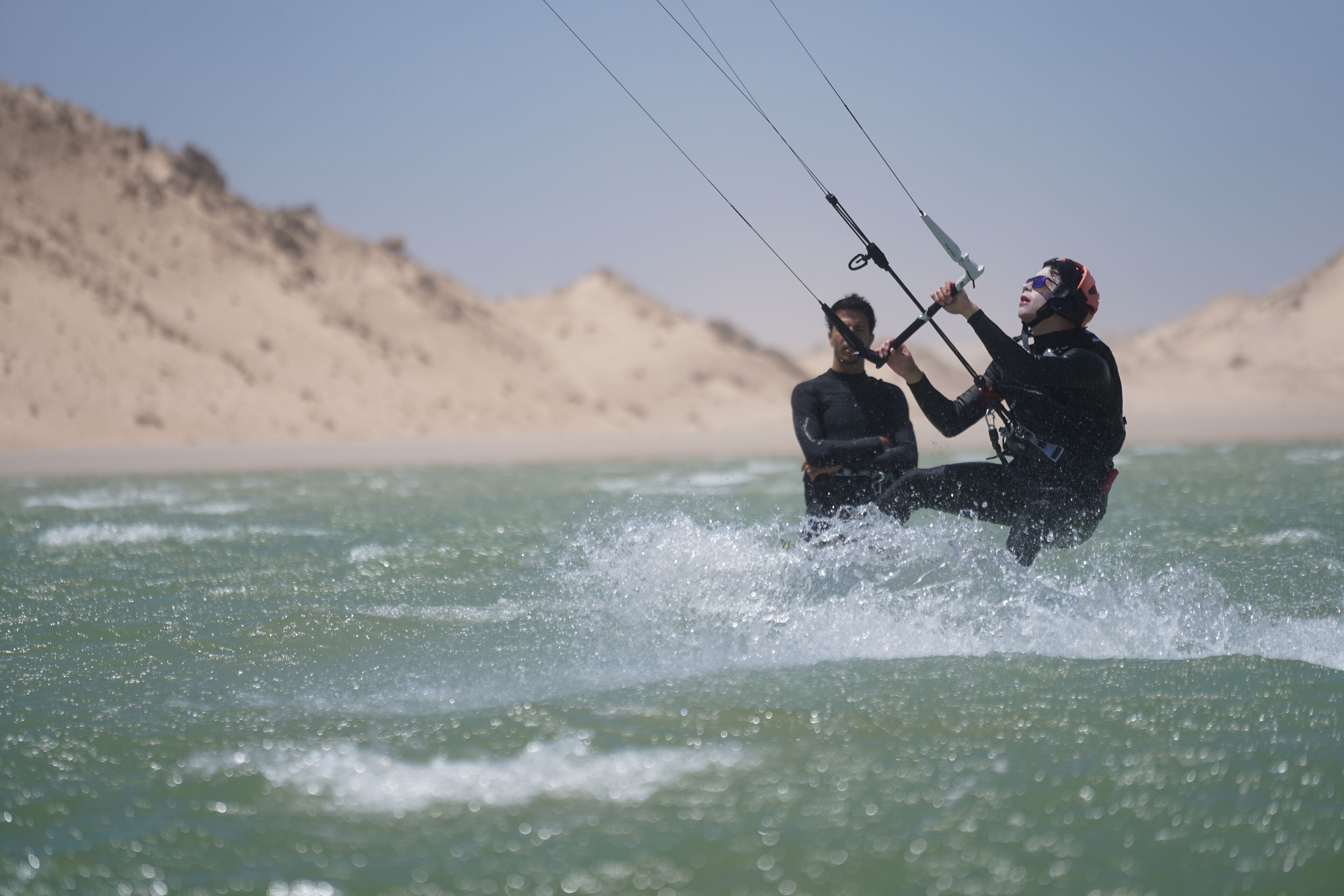 Two people kiteboarding in a body of water with a mountainous backdrop.