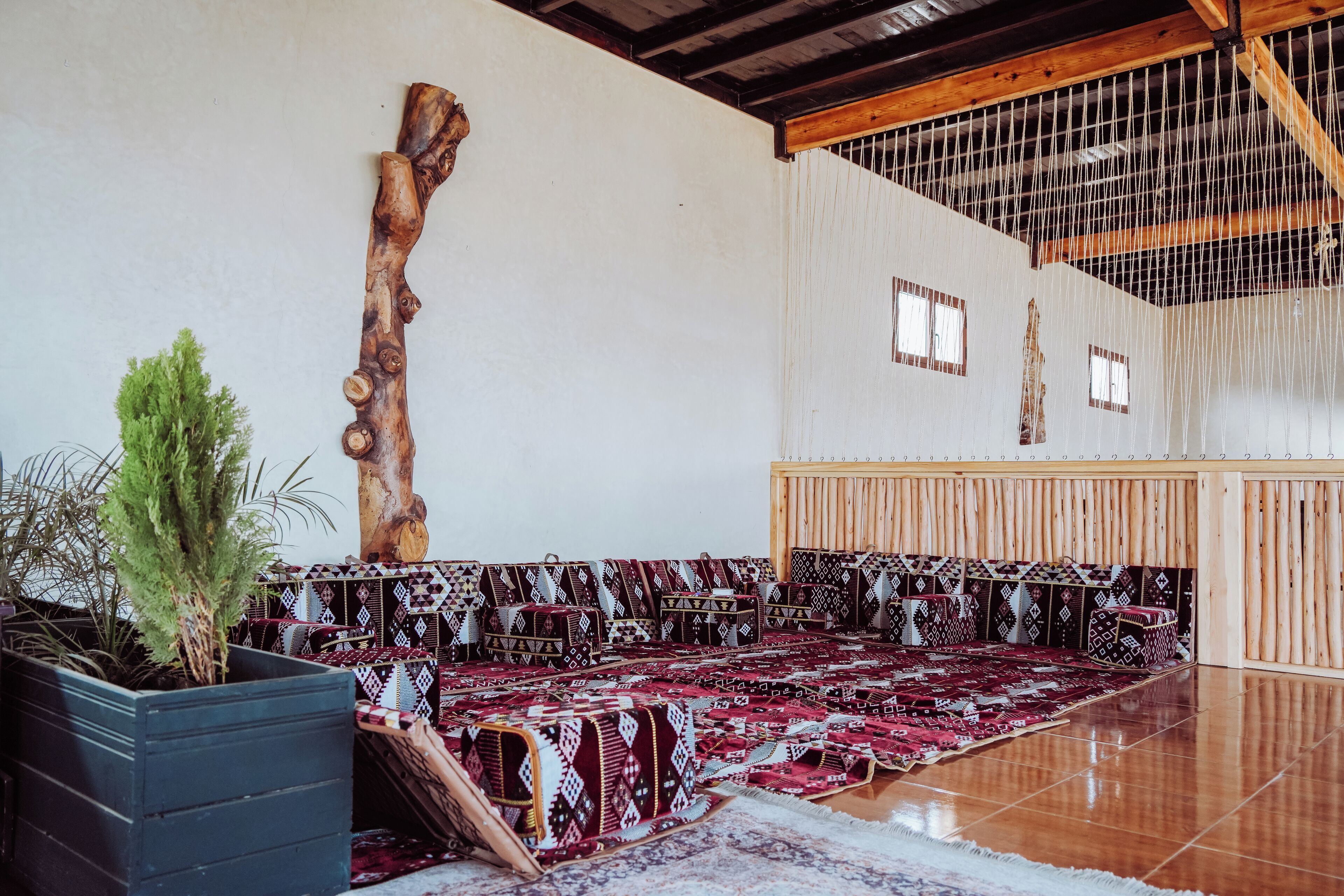 A spacious room with a high ceiling, wooden beams, a large wooden sculpture, patterned cushions, and a potted plant.