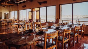 A restaurant with wooden tables and chairs, large windows with a view of the beach, and a rustic interior design. - NORTH LAGOON DAKHLA (Dakhla)