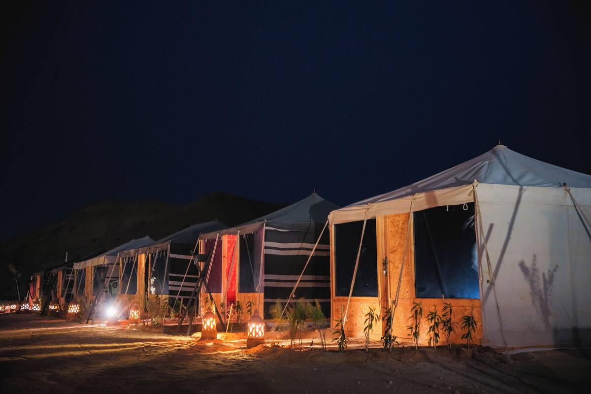 A row of tents with a dirt ground and some plants in front.