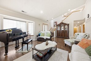 A living room with a grand piano, a sofa, a coffee table, and a staircase leading to another room.