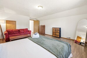 A bedroom with a bed, a red sofa, a wooden wardrobe, and a mirror.
