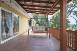 A covered porch with a swing set, a wooden railing, and a view of a house and trees.
