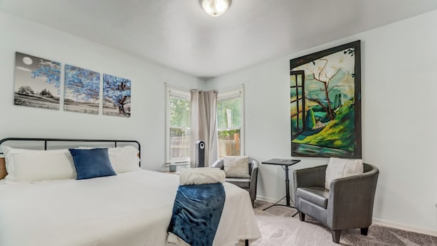 Une chambre à coucher avec un lit, deux chaises, une petite table et un grand tableau accroché au mur.