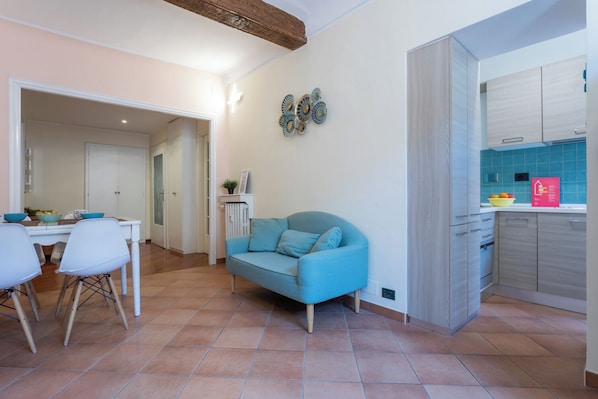 A modern living room with a blue sofa, a dining area with white chairs, and a kitchen with teal tiles. - Quartieri Central Home by Wonderful Italy (Turin)