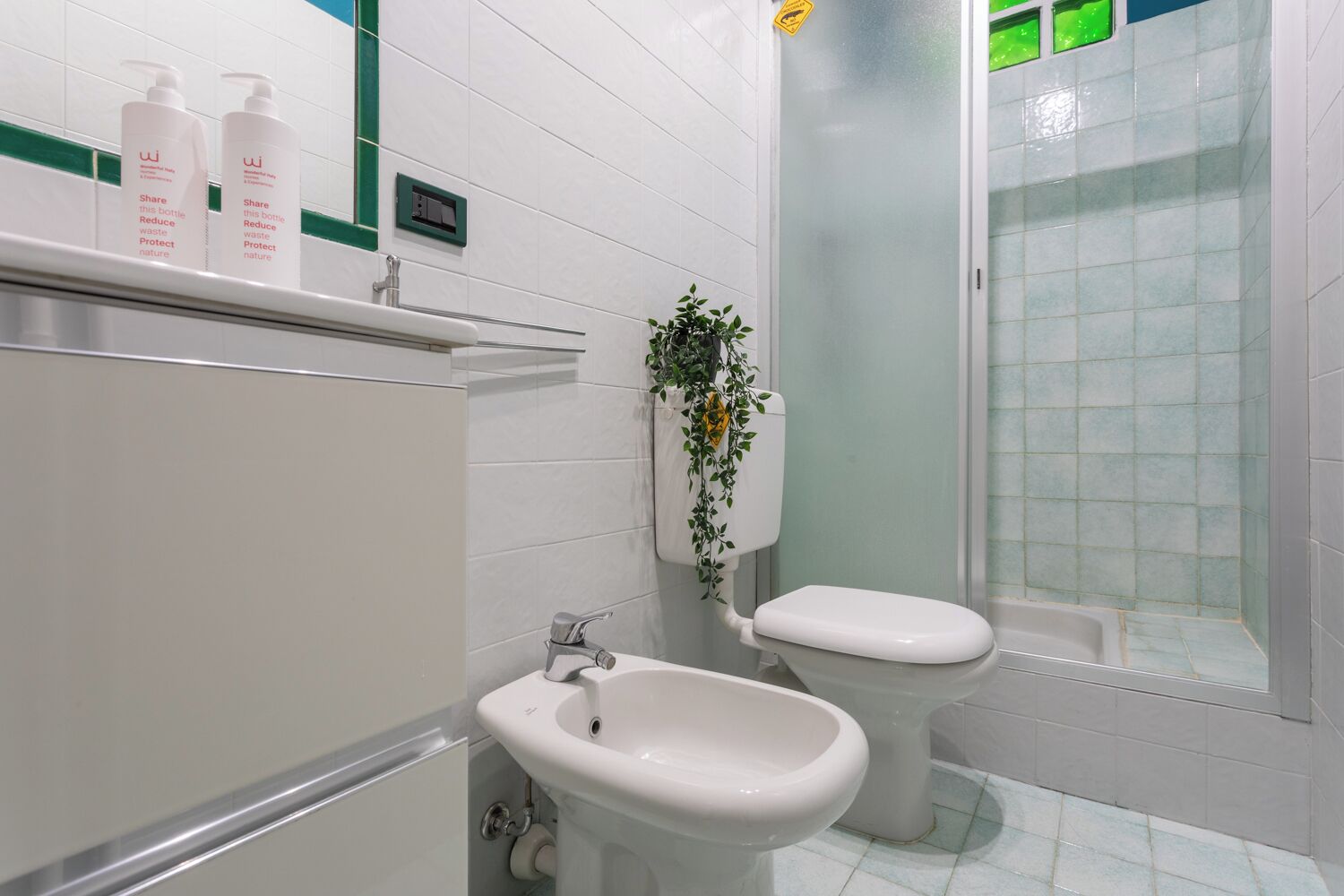 Ein modernes Badezimmer mit Toilette, Bidet und Waschbecken. Auf dem Regal über dem Waschbecken stehen zwei Flaschen.