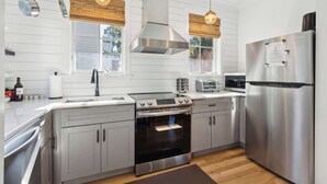 Une cuisine moderne dotée d’appareils électroménagers en acier inoxydable, de stores en bois et de luminaires suspendus.