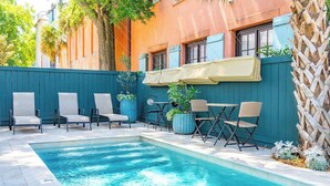 Un espace piscine agrémenté de chaises et d’une table, entouré d’une clôture bleue et d’un treillage en bois.
