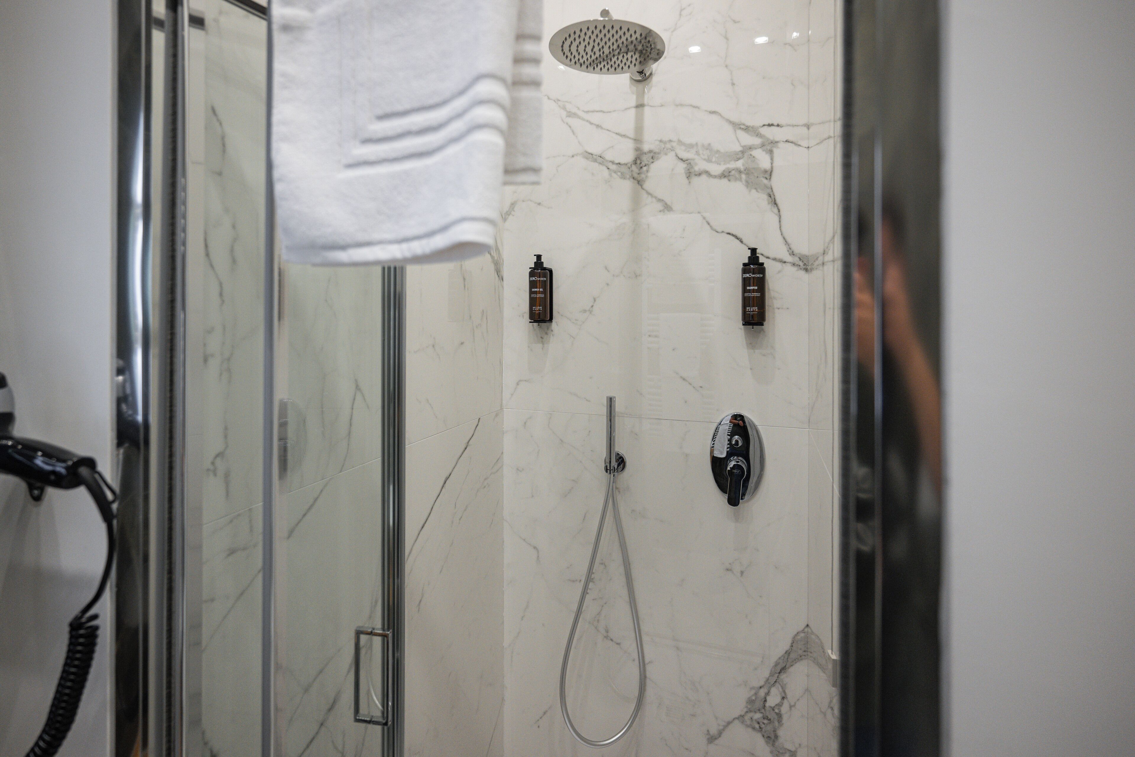 A modern bathroom with a glass shower enclosure, a handheld showerhead, and two wall-mounted showerheads.