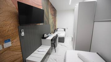 Una habitación de hotel moderna con un televisor de pantalla plana montado en la pared, un escritorio con una silla, una cama con almohada blanca y un armario.