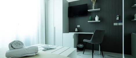 A modern hotel room with a bed, a desk, a chair, a TV, and a bathroom area.