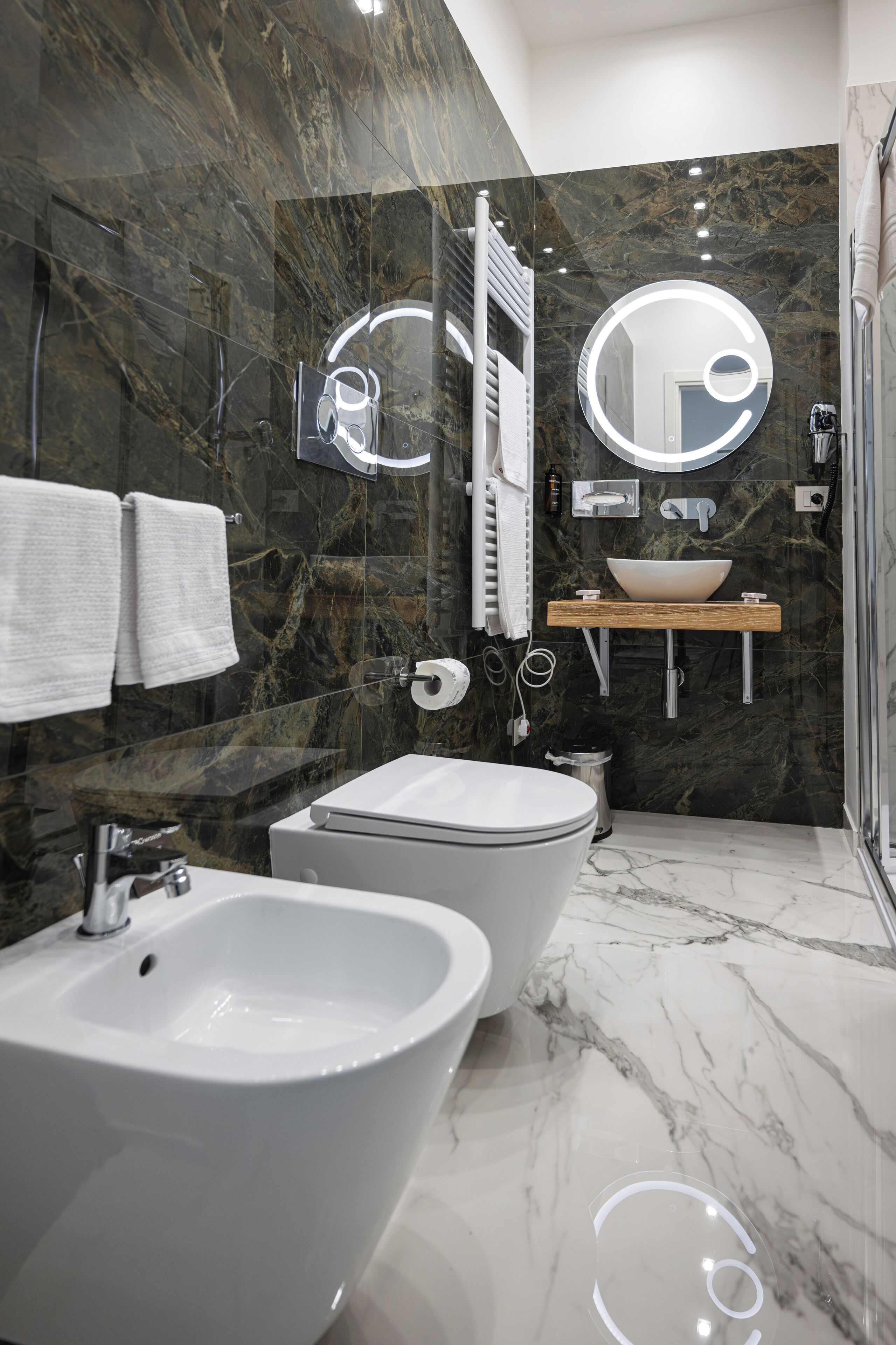 Une salle de bain moderne avec un mur en marbre, un grand miroir, un bidet et un lavabo.