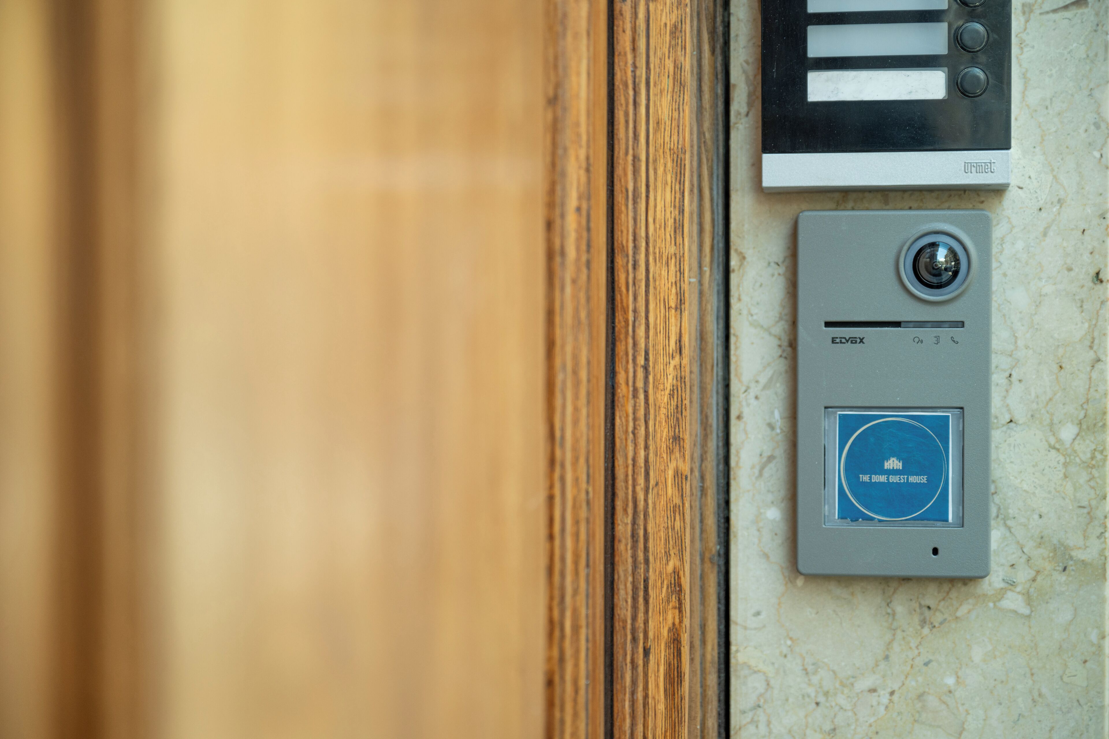 A door with a wooden frame, a wall-mounted intercom system, and a digital keycard reader labeled "THE GUEST HOUSE".