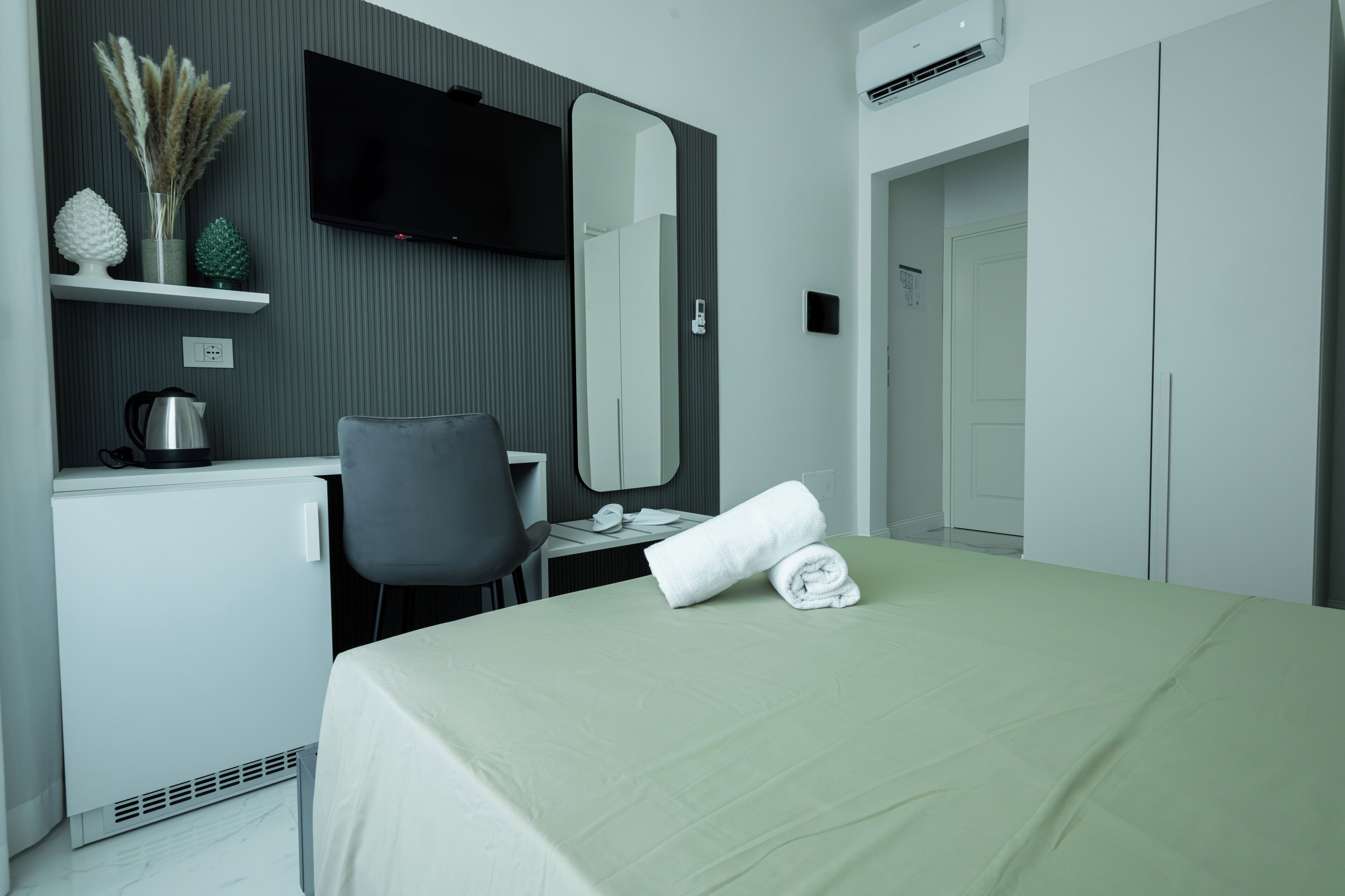 A hotel room with a bed, a desk, a chair, a television, a mirror, and a wardrobe.