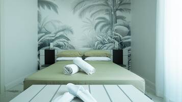 A hotel room with a bed, pillows, a rolled towel, and slippers on a table.