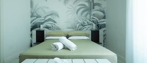 Une chambre d’hôtel avec un lit, des oreillers, une serviette roulée et des chaussons sur une table.