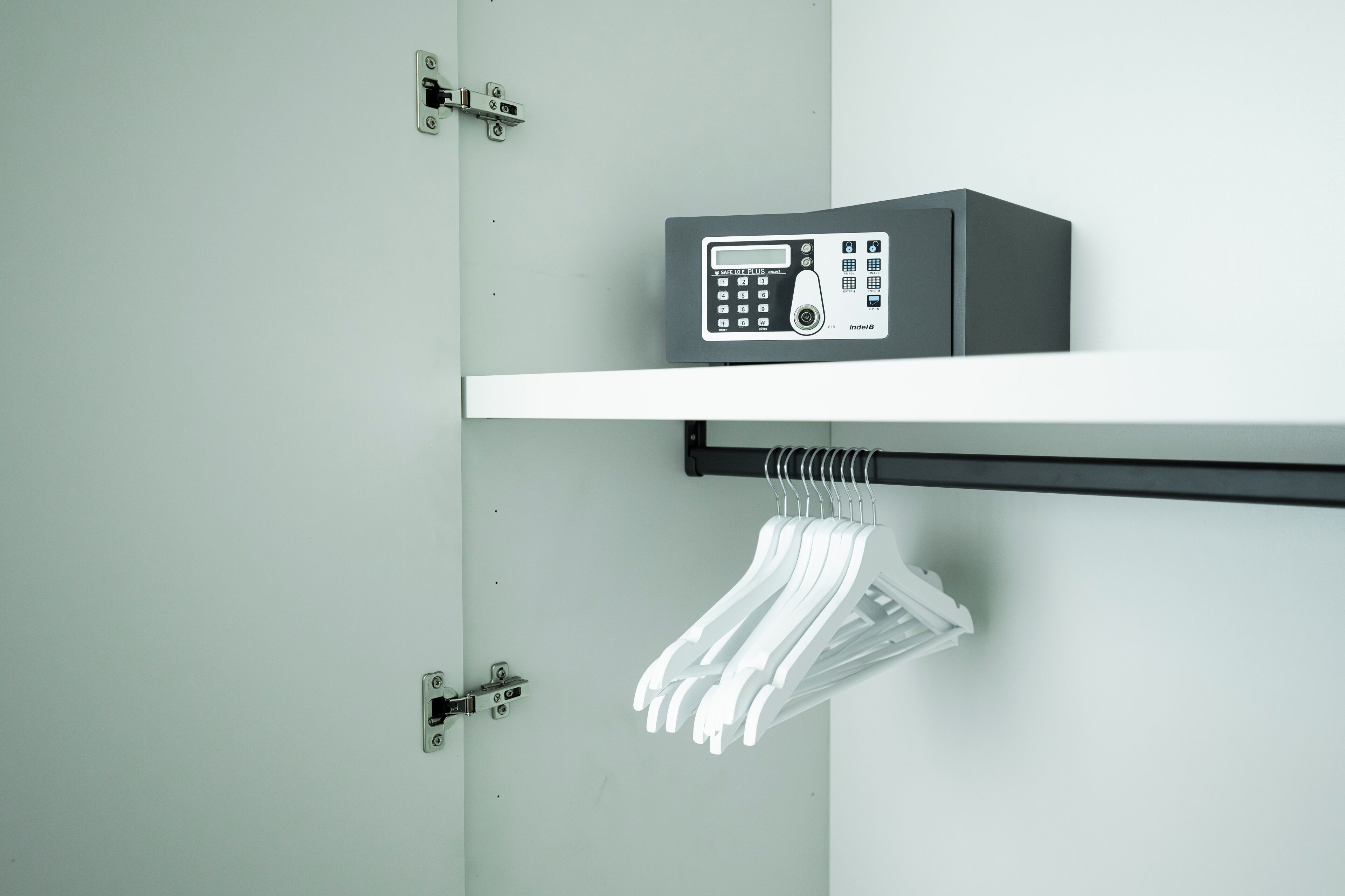 A room with a white wall, a black shelf with a security keypad, and a white hanger rack.