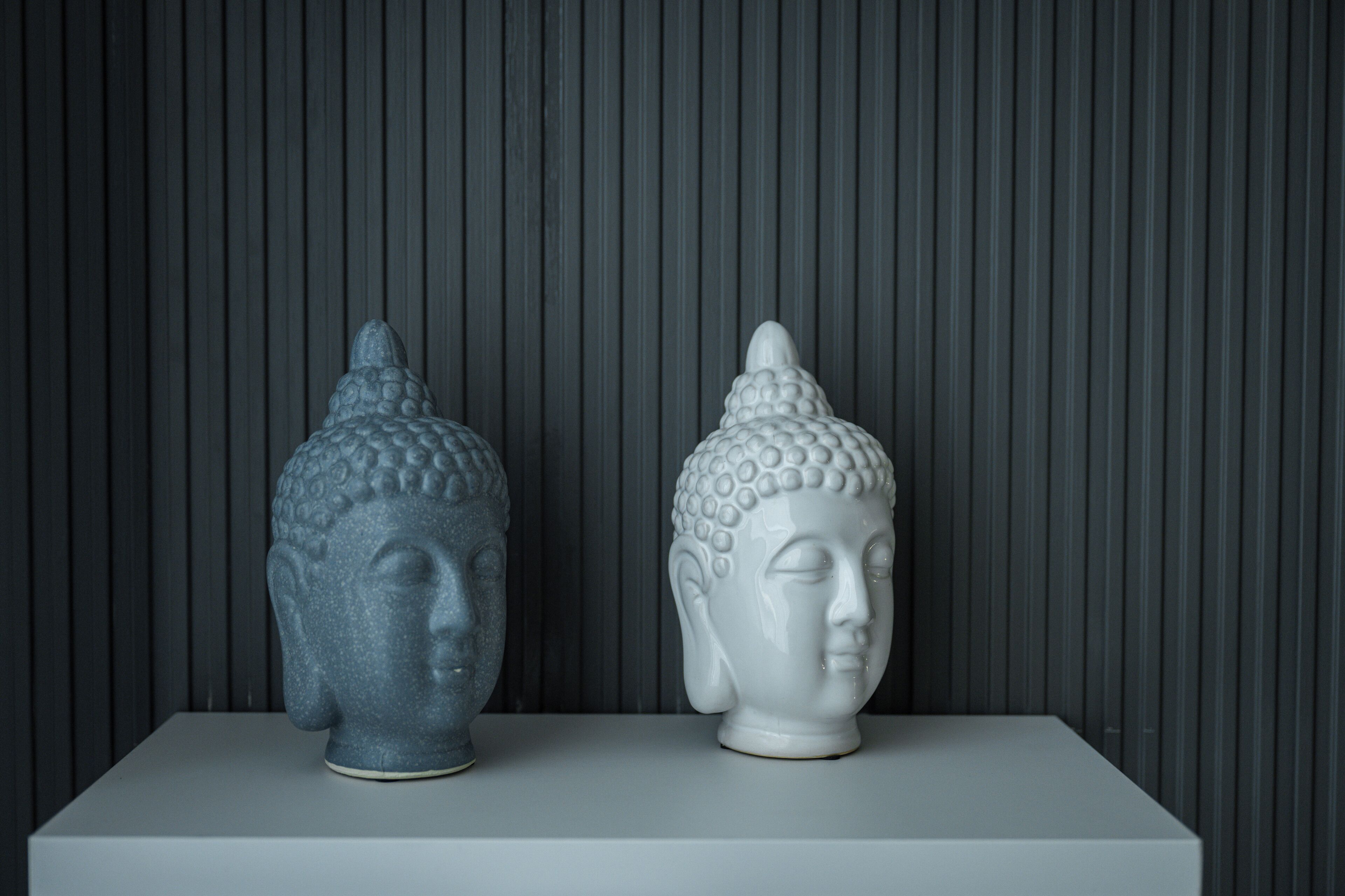 Two Buddha statues on a white pedestal against a vertical striped background.