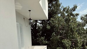 A small outdoor balcony with a white wall, a black wicker table, two wicker chairs, and a potted plant. - Cozy 2-bedroom apartment in small place Ostrvica near Omiš (Ostrvica)