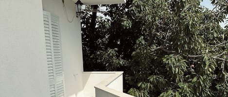Ein kleiner Balkon mit einer weißen Wand, einem schwarzen Korbstuhl-Tisch und zwei Korbstühlen sowie einem Blumentopf.