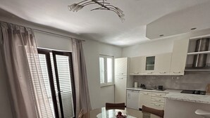 A modern kitchen with white cabinets, a dining area with a round table and wicker chairs, and a ceiling light fixture. - Cozy 2-bedroom apartment in small place Ostrvica near Omiš (Ostrvica)