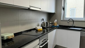 A modern kitchen with white cabinets, a black countertop, a built-in oven, and a window with a view.