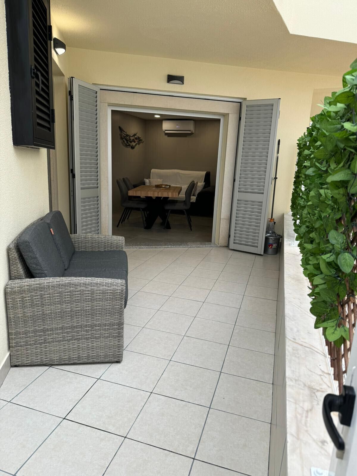 Un patio con un sofá gris, una mesa de comedor con sillas y una planta en maceta.