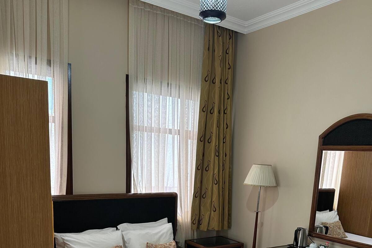 A hotel room with a large bed, a bedside table with a lamp, a dresser, and a mirror.