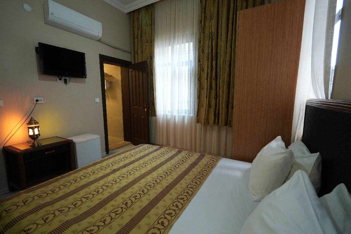 A hotel room with a bed, a television, a lamp, and a window with curtains.